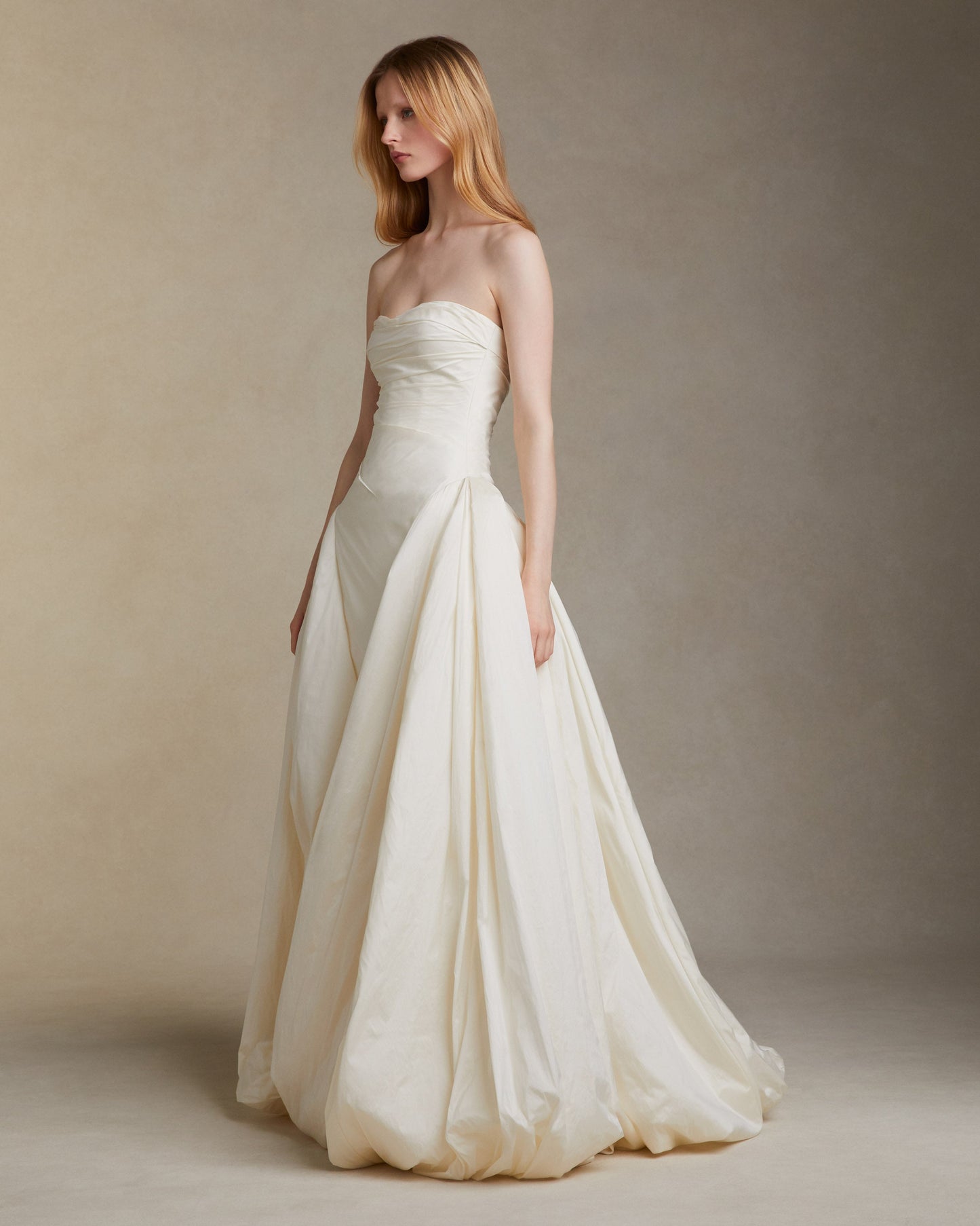 Woman wearing a strapless white wedding dress against a plain background