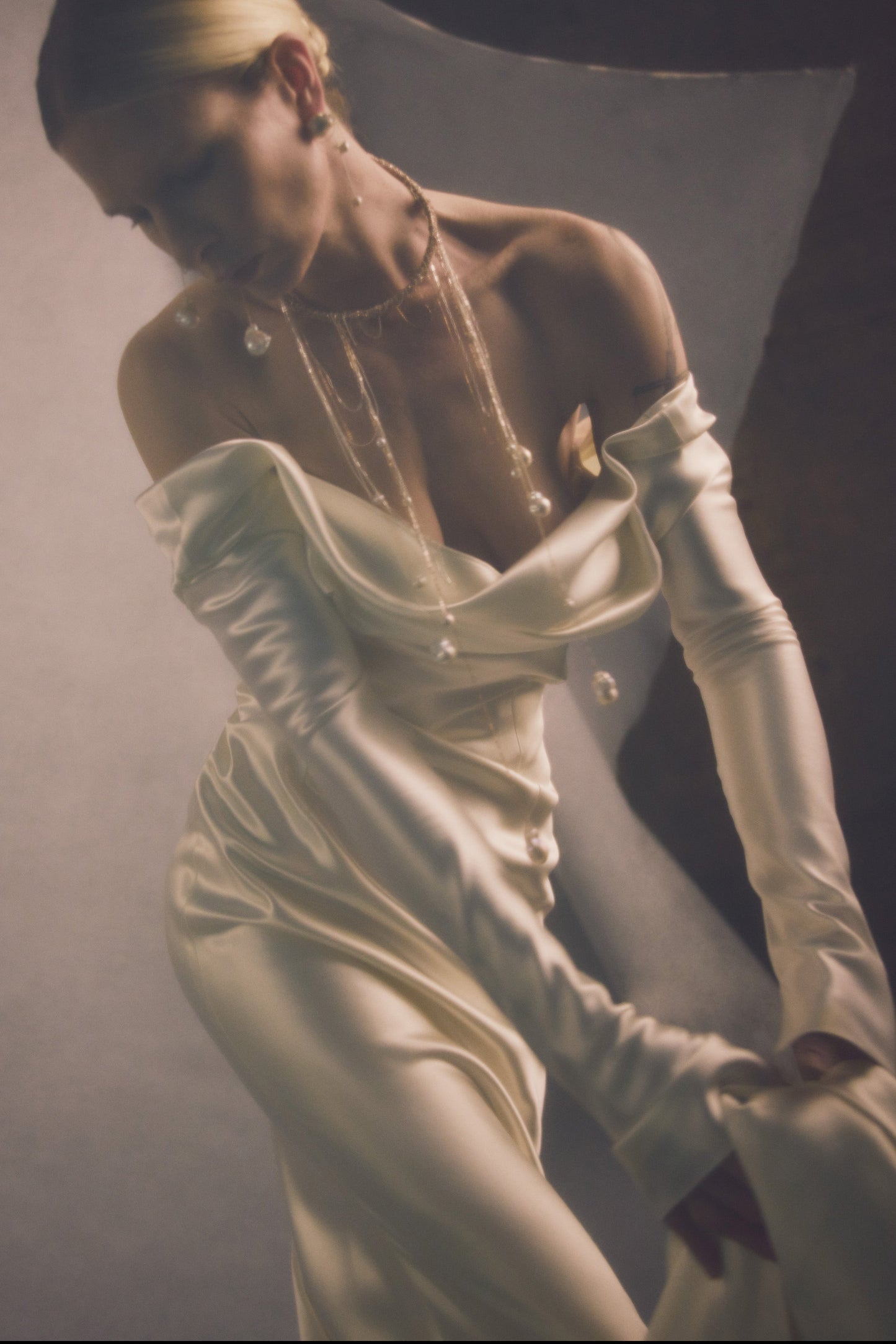 Model wearing Noa off-shoulder long sleeve bias cut silk wool gown with draped neckline and sheer pearl necklace