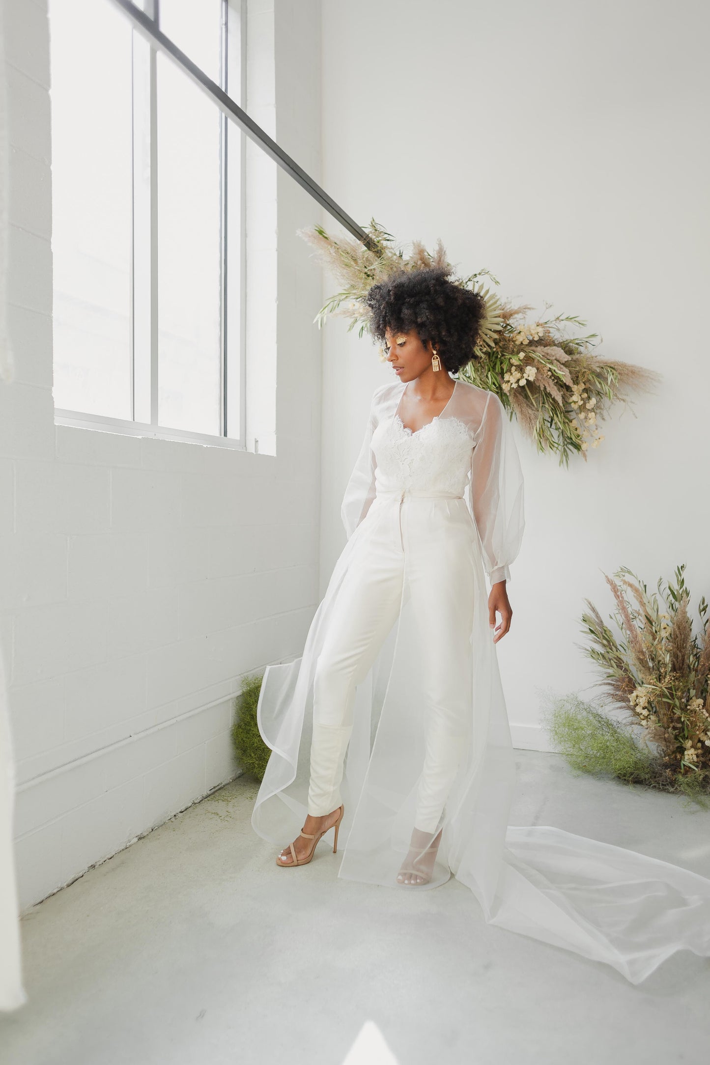 Woman in a white wedding dress standing in a minimalistic room with large windows and decorative plants.