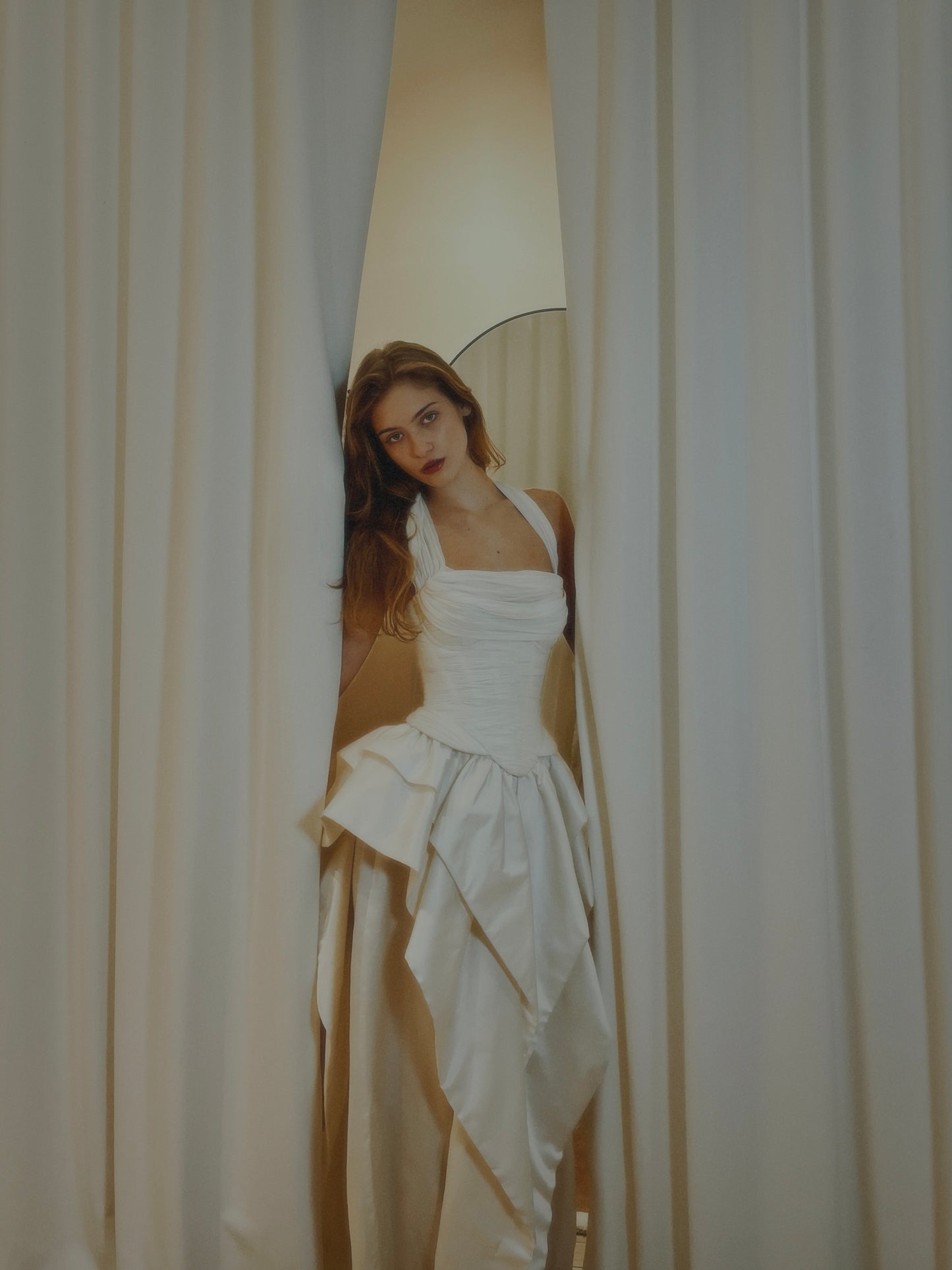 Woman in a white dress standing behind a curtain