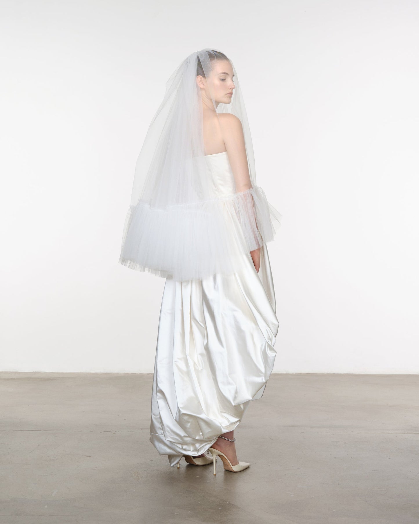 Woman wearing a white wedding dress with a veil and gloves on a plain background