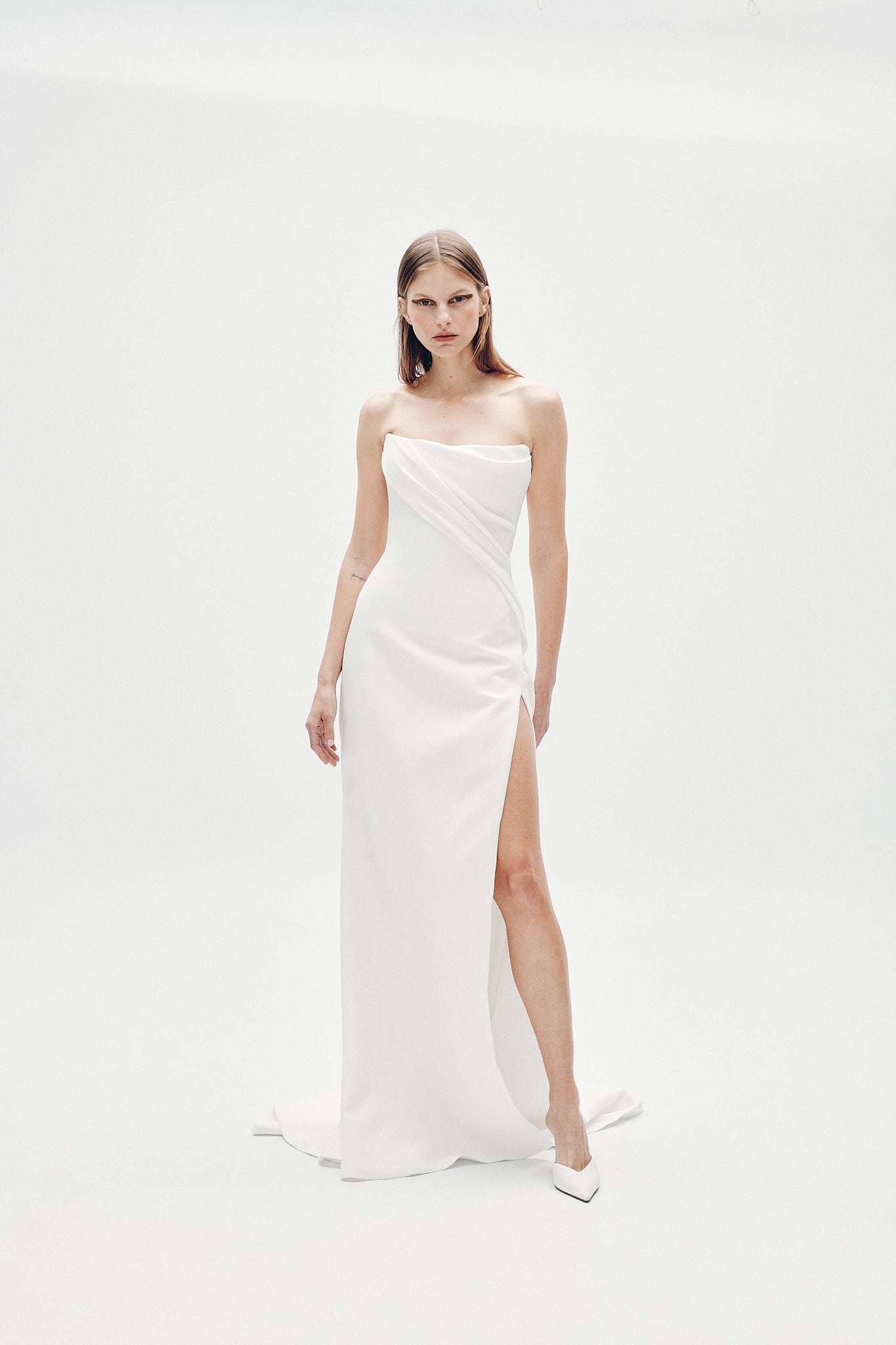 Woman wearing a white strapless gown with a slit on a white background