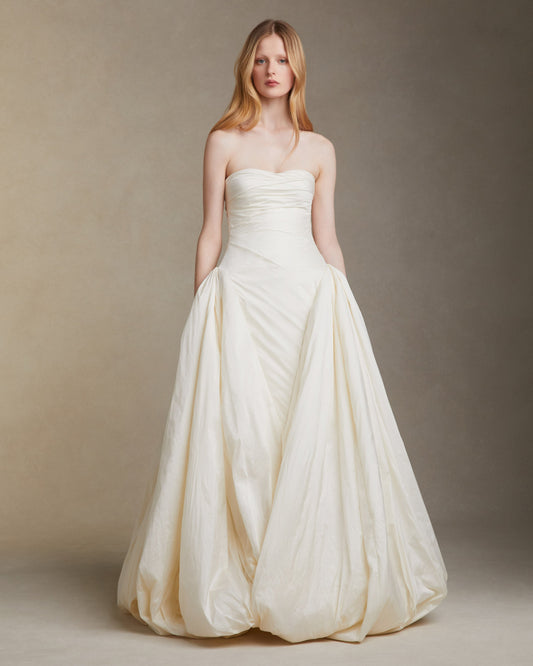 Woman wearing a strapless white wedding dress against a plain background