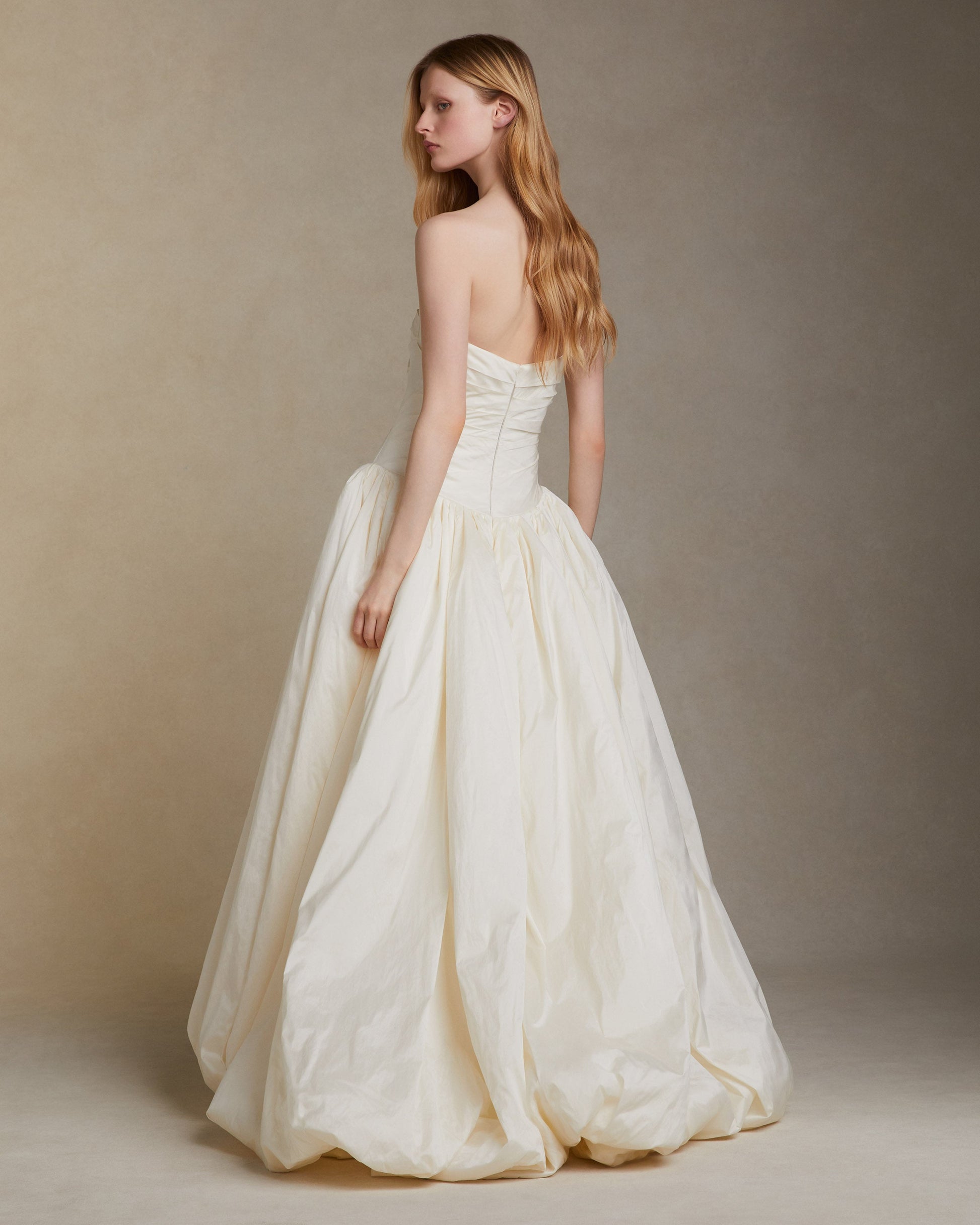 Model wearing the Bex Tissue Taffeta strapless gown with elongated V waist and bubble hem skirt against a neutral background