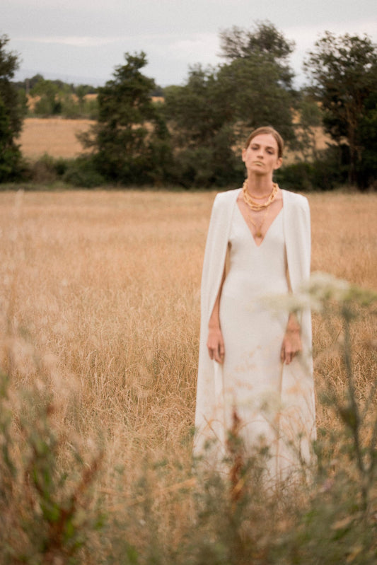 Model wearing the Bhristy cape in a natural field setting with double crepe fabric and clean, elegant lines