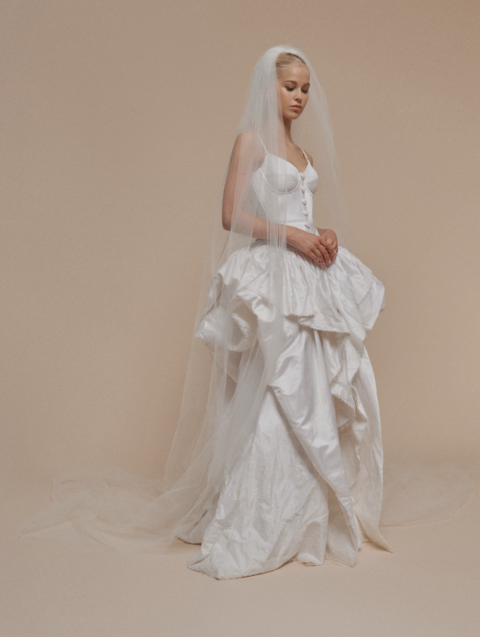 Woman wearing a white wedding dress with a long train and veil on a beige background
