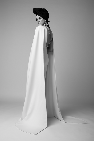 Model wearing the Blanche white crepe gown with dramatic long sleeves and low back against a plain studio background