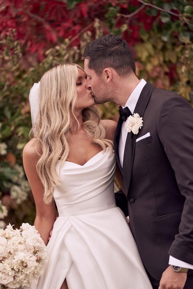 Man and woman in wedding attire kissing in front of a floral background