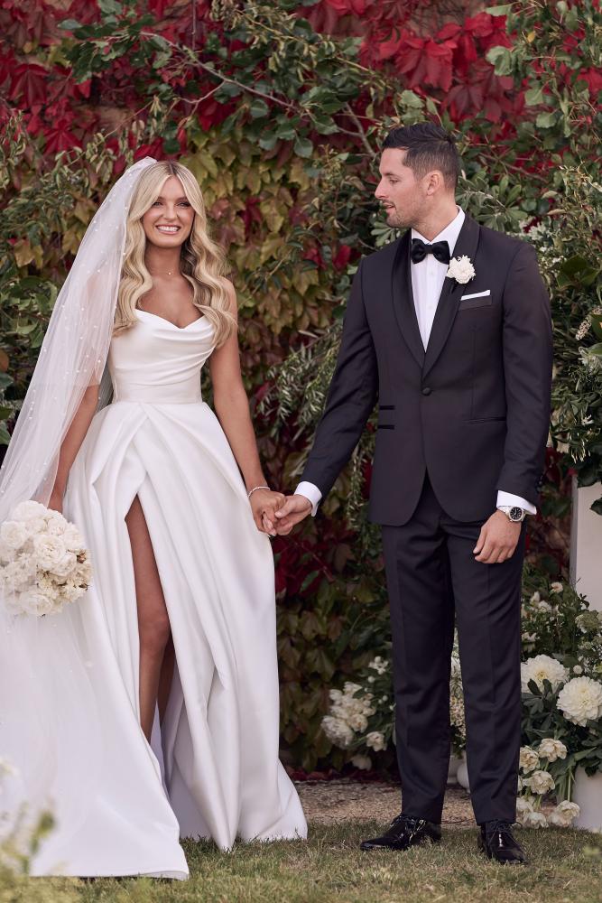 Man and woman in wedding attire standing together with a decorated background