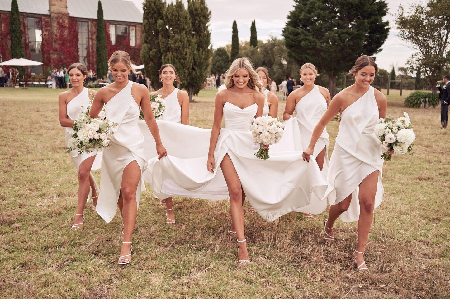 Bride wearing strapless Chantelle ballgown with sweetheart bodice and asymmetrical slit walking with bridesmaids outdoors