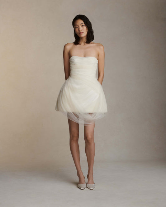 Model wearing the strapless Bernie white structured Cady mini dress with draped tulle overlay against neutral background