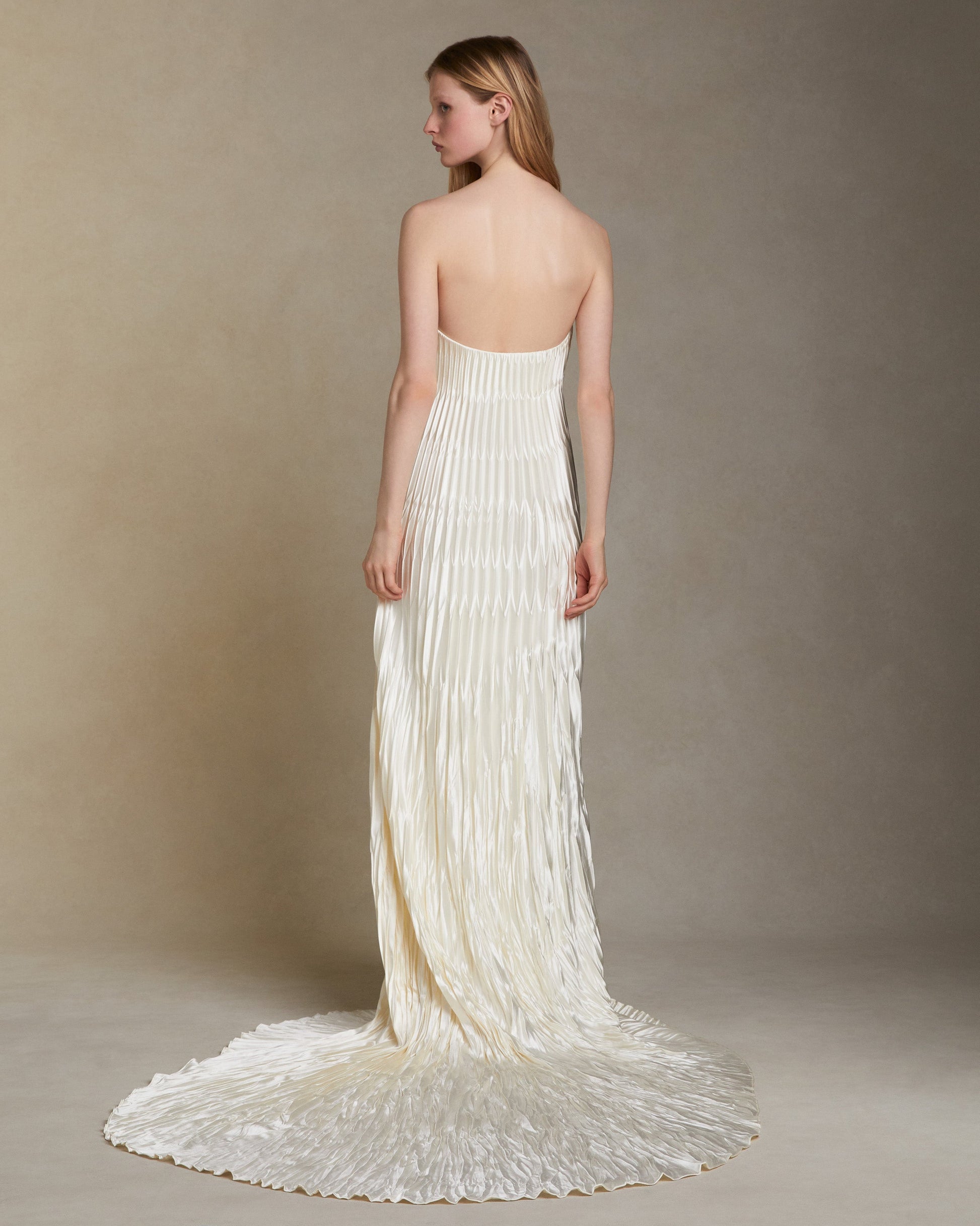 Woman wearing a strapless, flowing white gown against a plain background