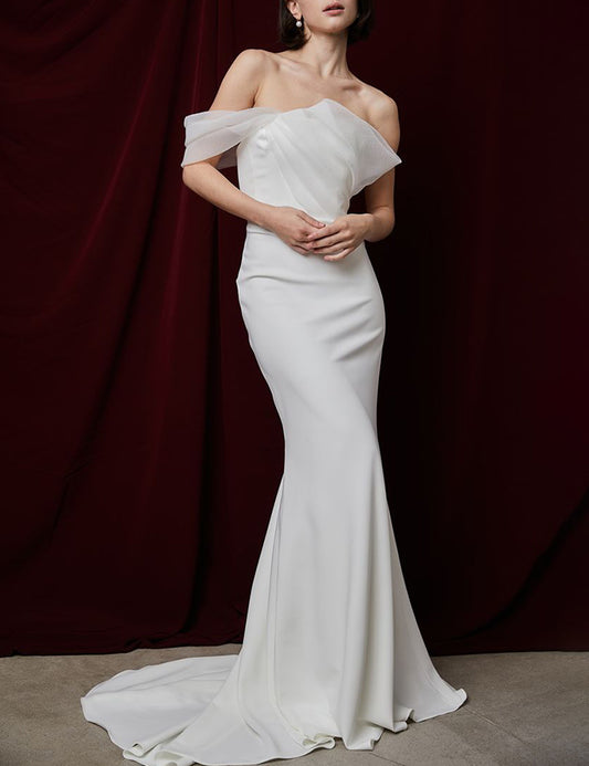 Model wearing the Destiny asymmetrical one-shoulder bias-cut white dress with draped detail and floor-length train against dark backdrop