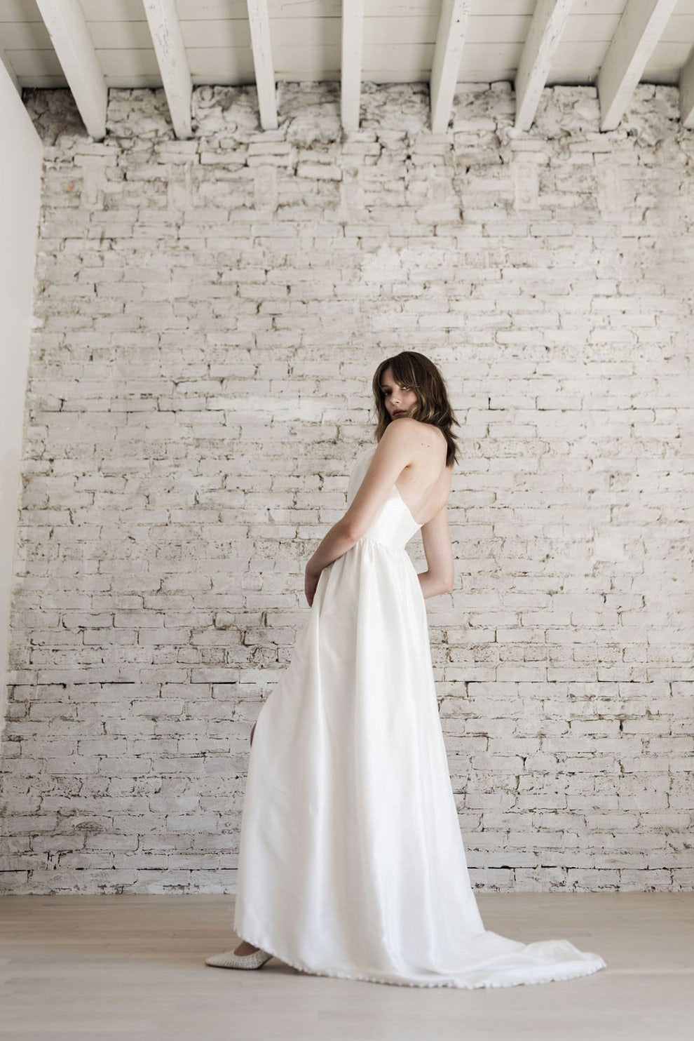 Woman in a white dress standing against a white brick wall.