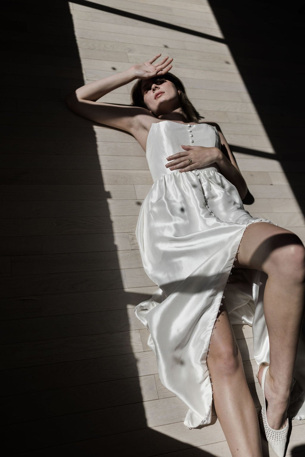 Woman in a white dress standing in a sunlit room with wooden floor.