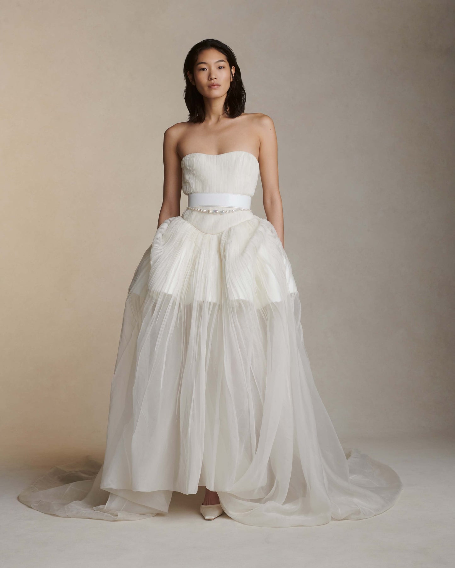 Woman wearing a strapless white wedding dress with a layered skirt against a neutral background