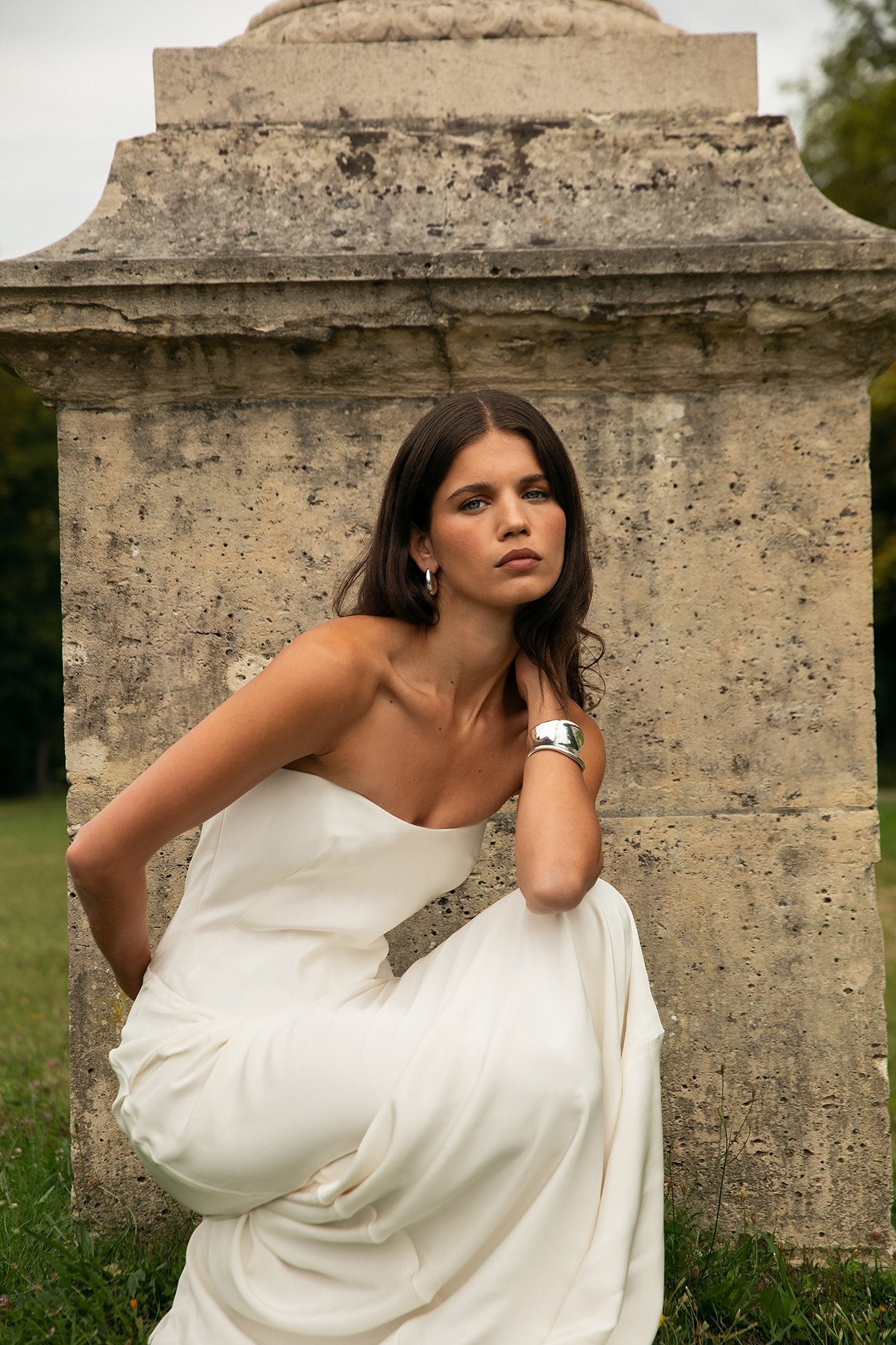 Woman in a white dress standing in front of an old stone monument.