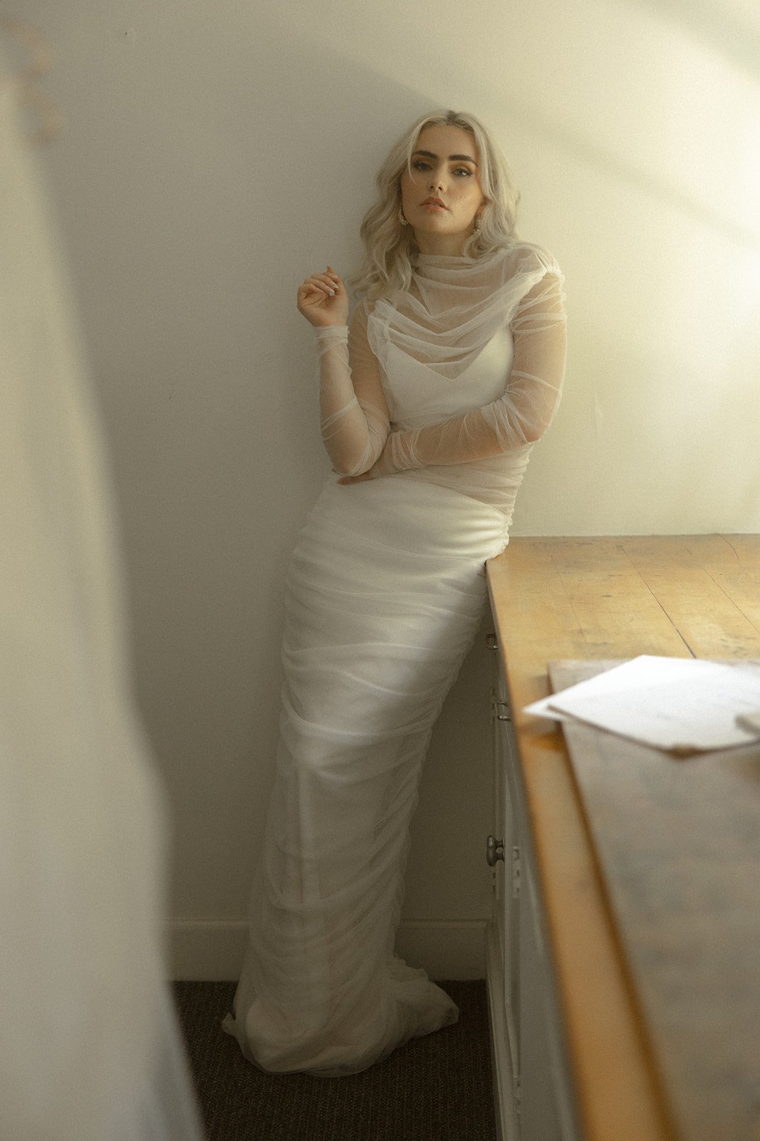 Person wearing a white outfit with sheer sleeves in a room.