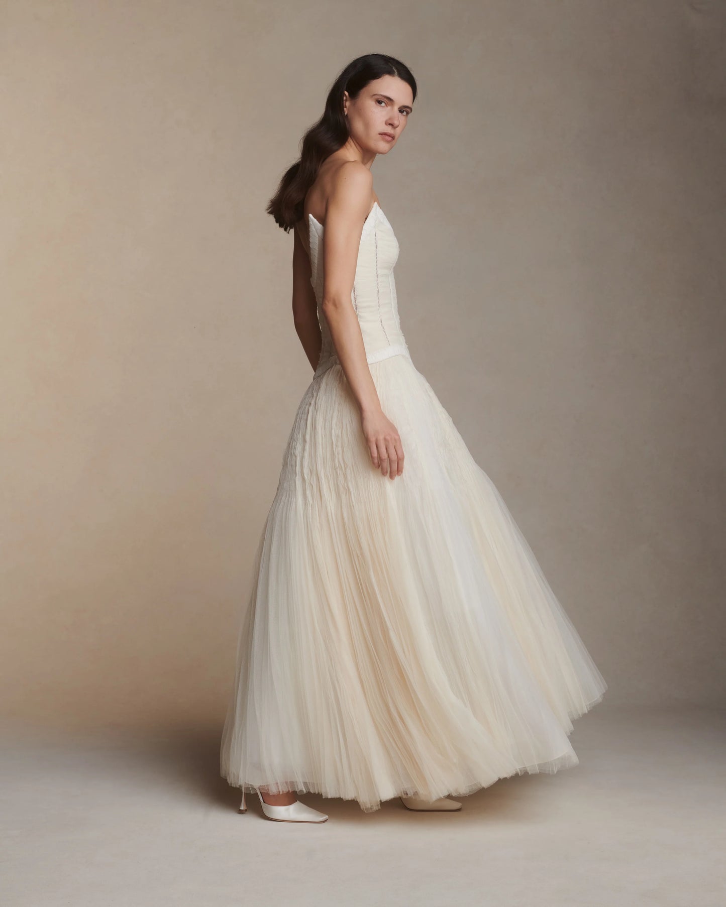 Woman wearing a white strapless gown against a beige background
