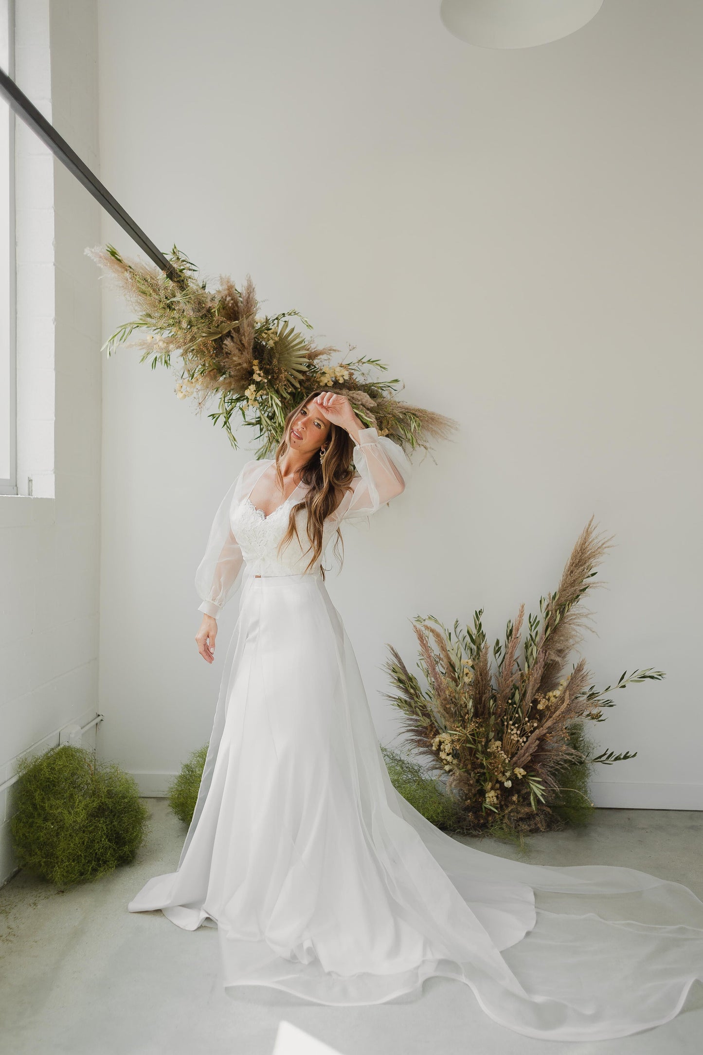 Woman in a white wedding dress standing in a minimalistic room with decorative plants.