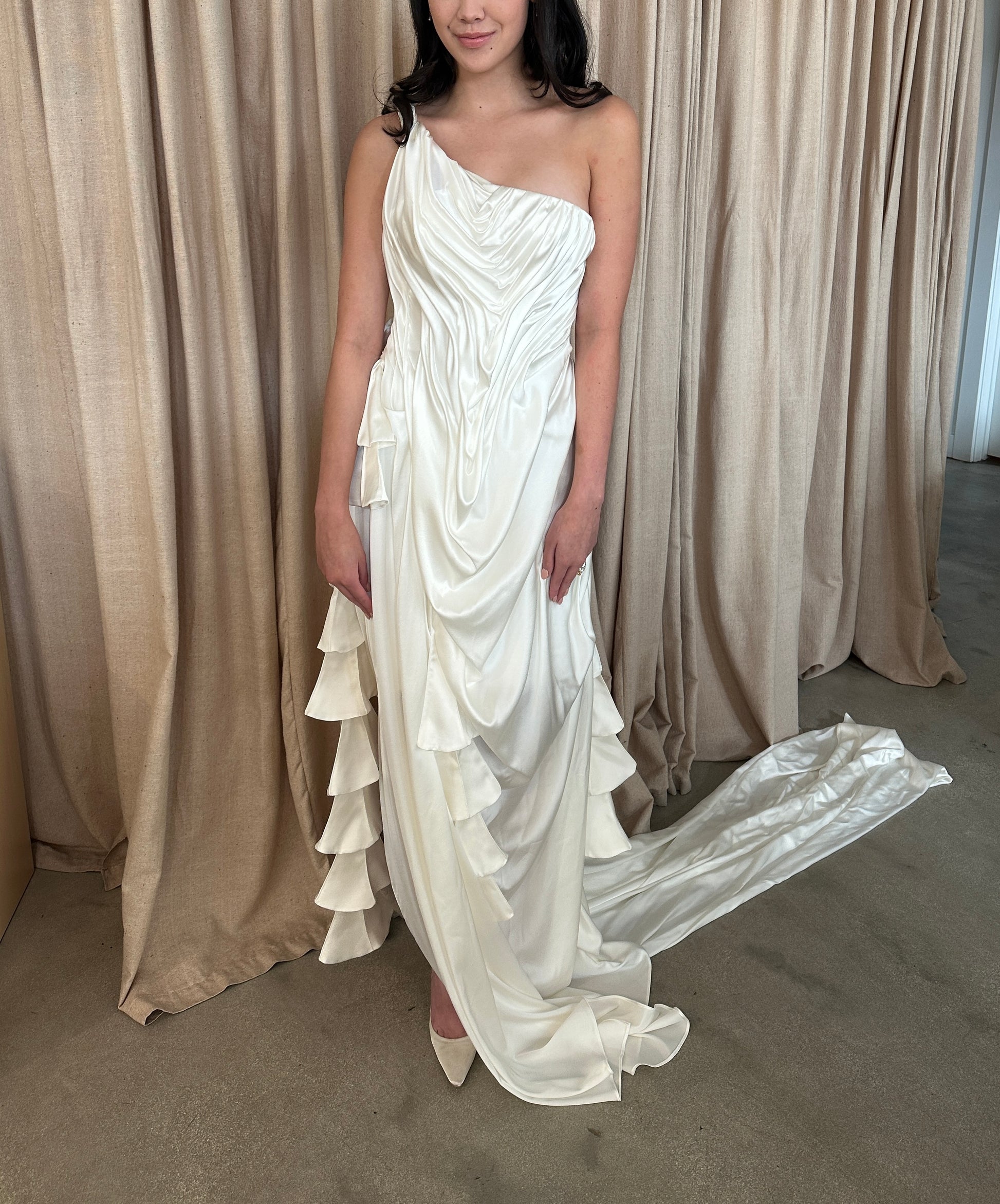 Model wearing the Silk Spring Awakening one-shoulder silk gown with intricate draping and cascading ruffles in a neutral studio setting