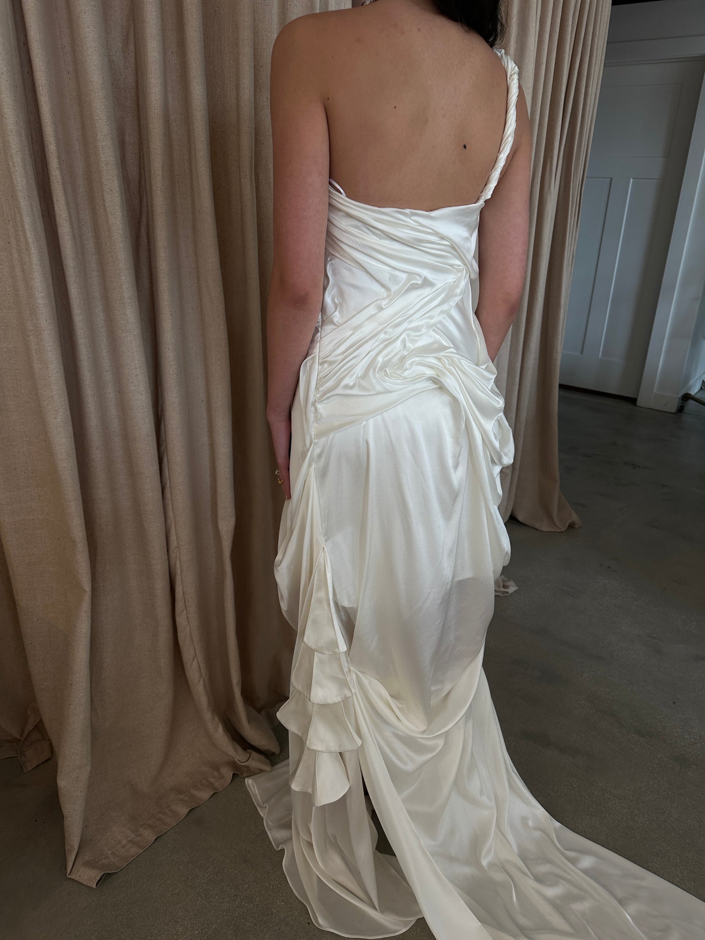 Model wearing the silk Spring Awakening gown with intricate draping and a single twisted shoulder strap in an indoor setting