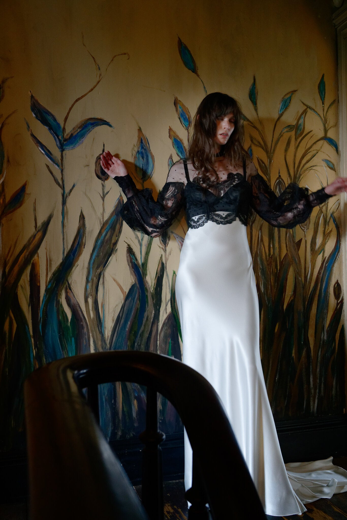 Model wearing the Victorian inspired black scallop lace balloon sleeve Izzie Topper over a white satin dress indoors