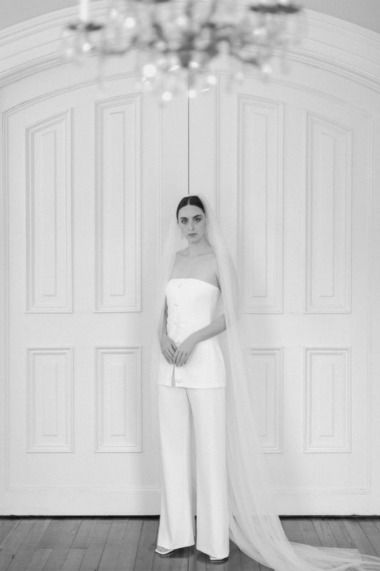 Model wearing white wide-leg James pant with strapless buttoned top and long veil in classic indoor setting