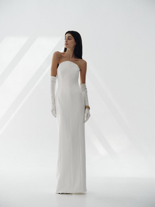 Model wearing the Jane strapless white crepe dress with straight skirt and long gloves in a bright minimalist studio