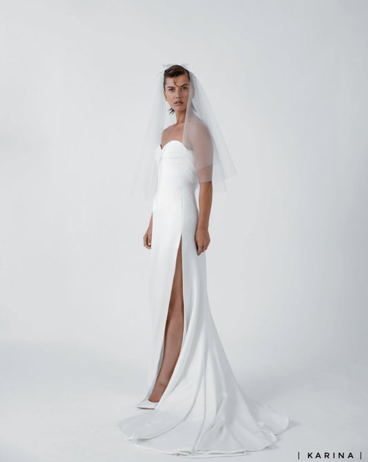 Model wearing the Karina white wedding dress with rounded sweetheart neckline and side slit in minimalist studio setting