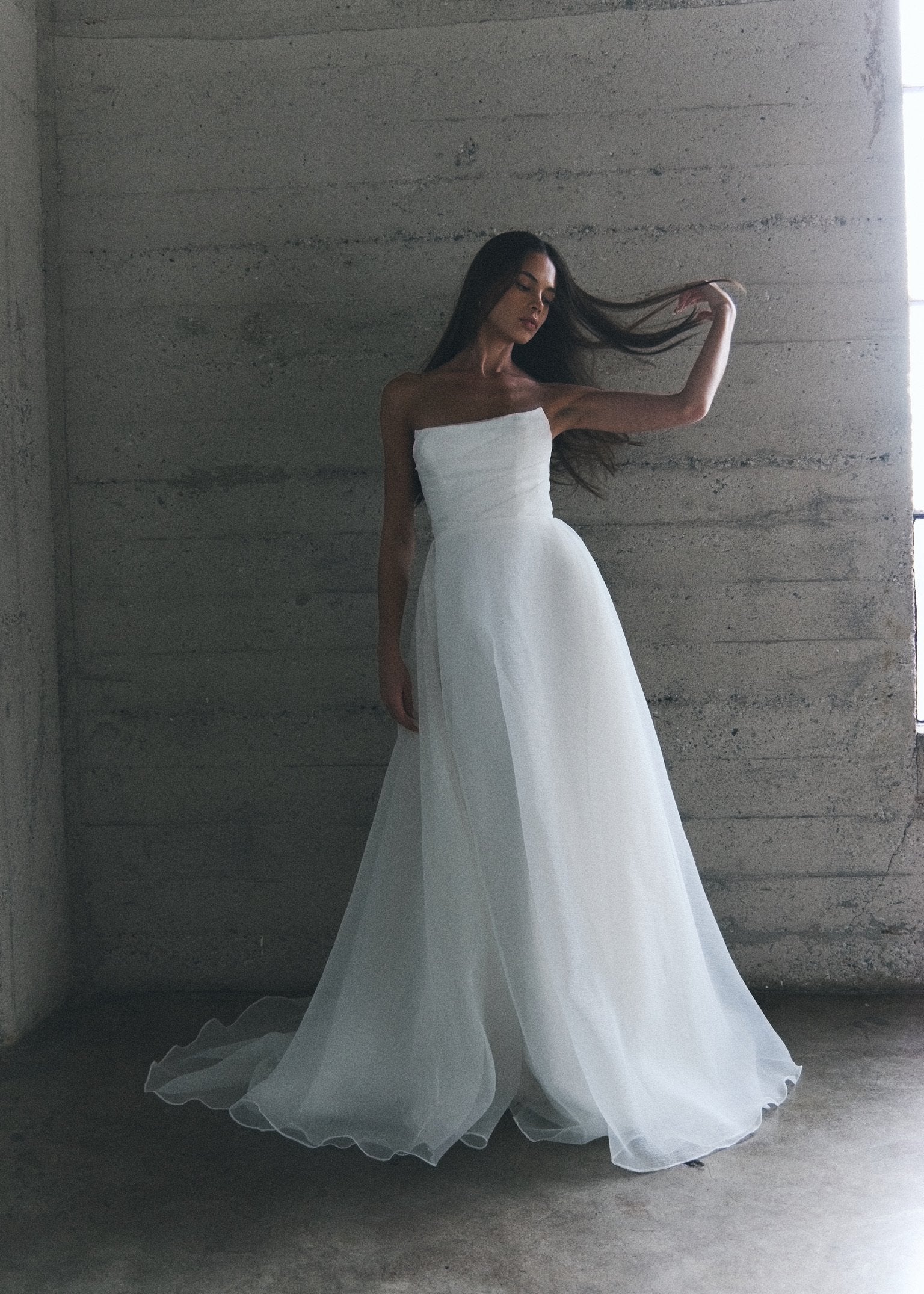 Model wearing the Liv white strapless A-line gown with textured organza overlay standing against a concrete wall