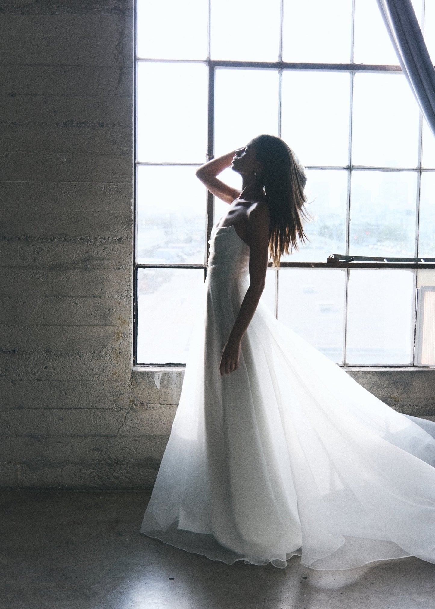 Model wearing Liv A-line wedding dress with textured organza overlay and pearl strap in soft natural light by window