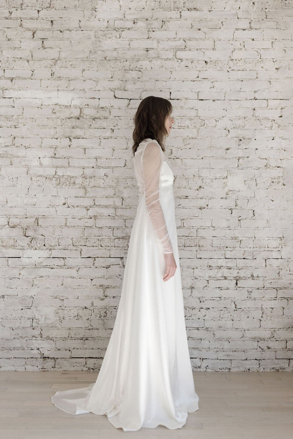 Woman in a white wedding dress standing against a light brick wall.