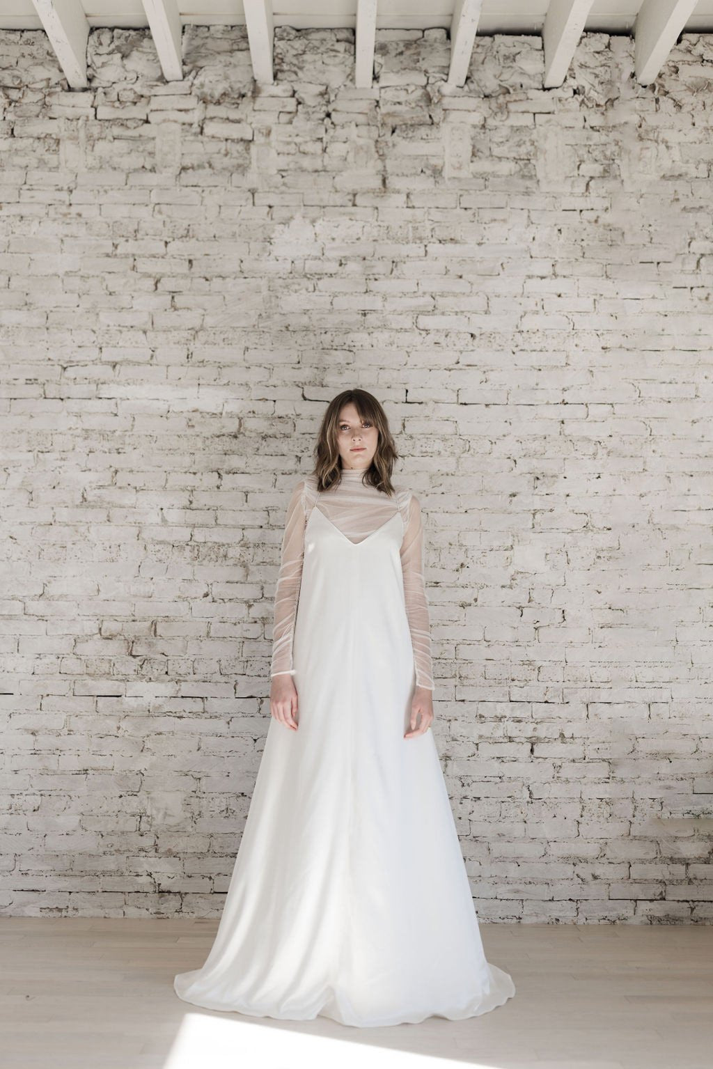 Woman in a white wedding dress standing against a white brick wall.