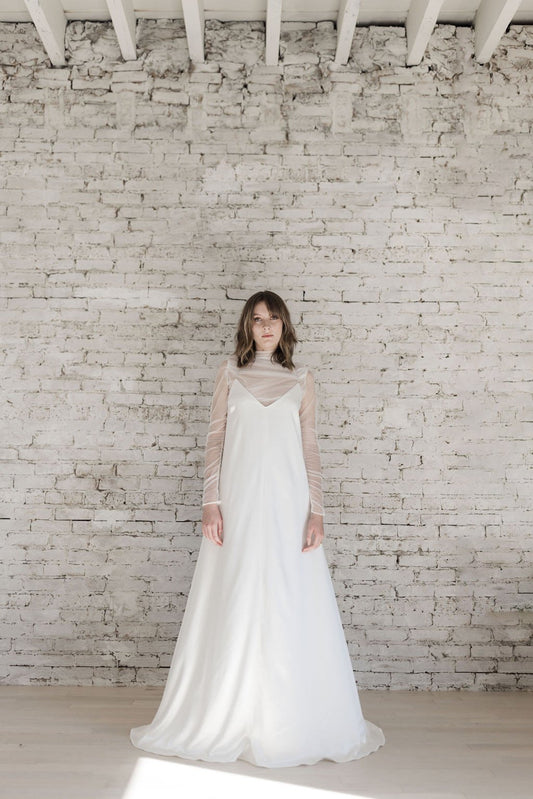 Woman in a white wedding dress standing against a white brick wall.