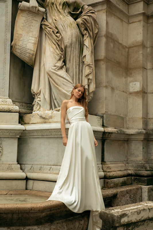 Woman in a white dress standing next to a classical statue in an outdoor setting