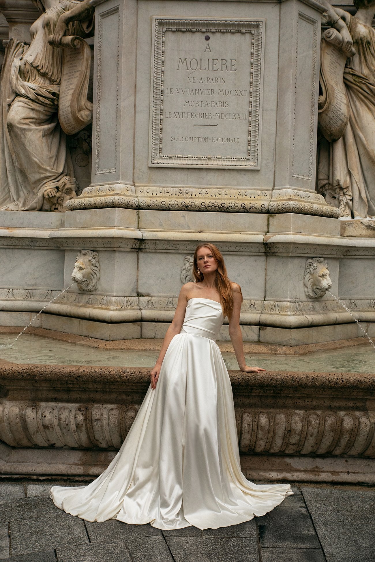 Woman in a white dress sitting on stone steps in front of a classical sculpture