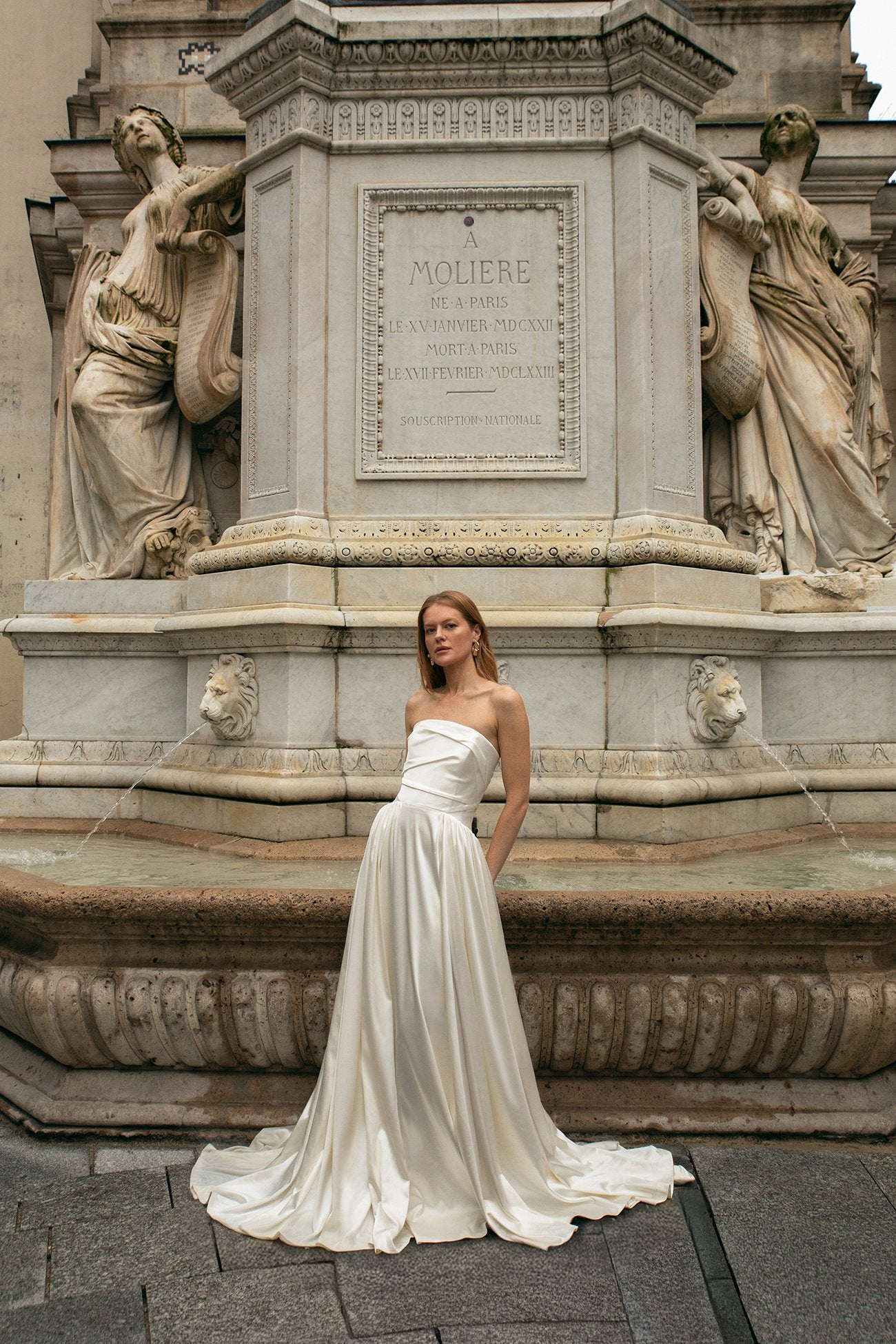 Woman in a white strapless gown standing in front of a classical statue and monument.