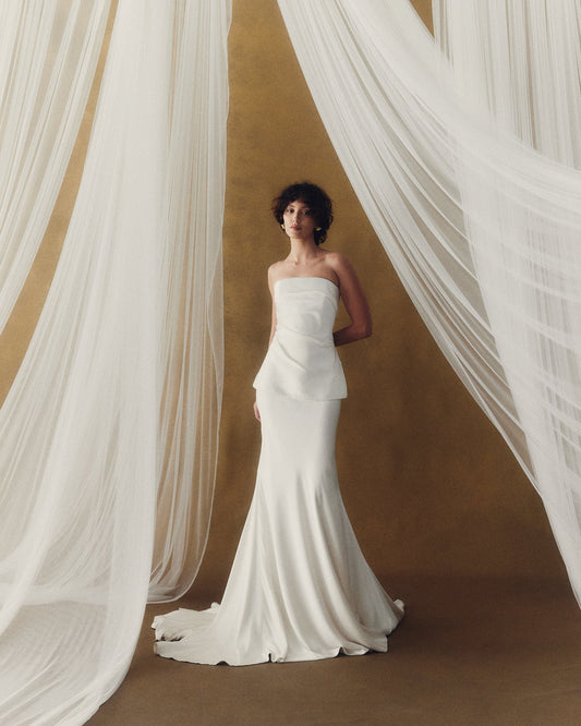 Model wearing the Mika white strapless corset dress with dropped waist and bell shape skirt against a neutral backdrop