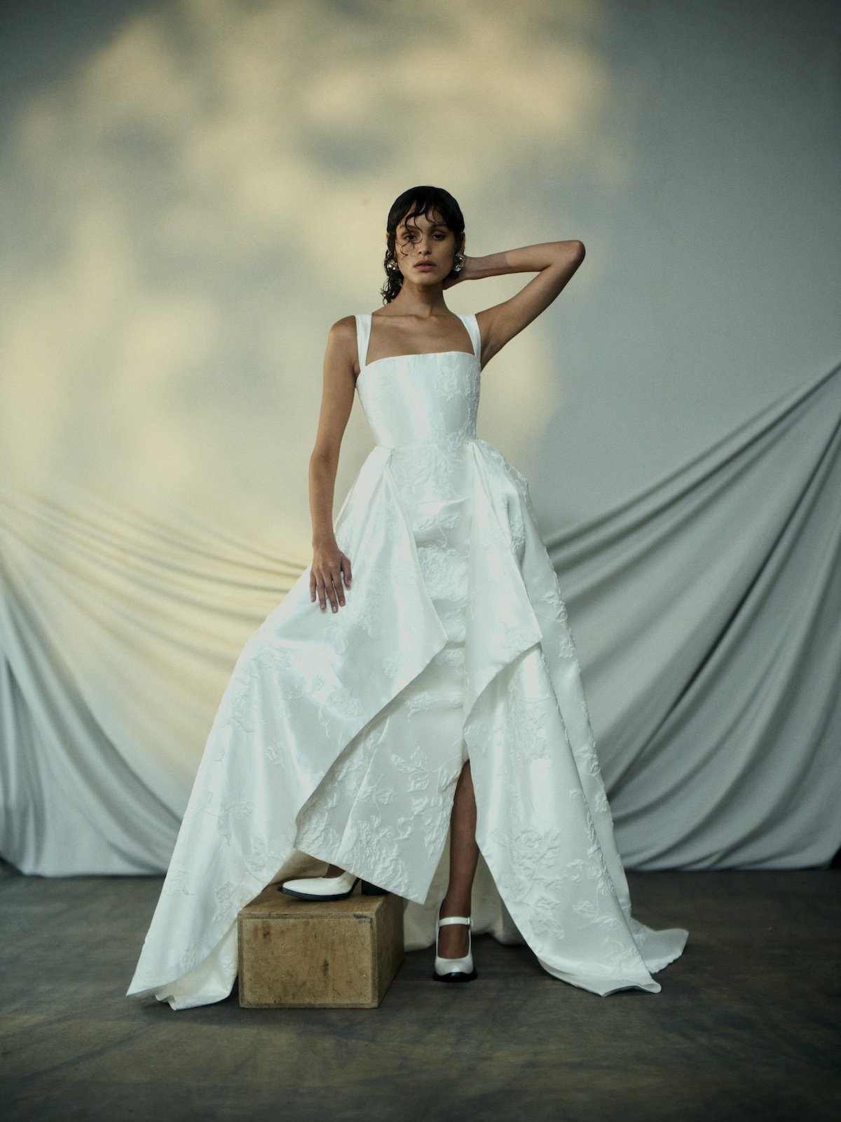 Woman in a white wedding dress standing on a box with draped fabric in the background