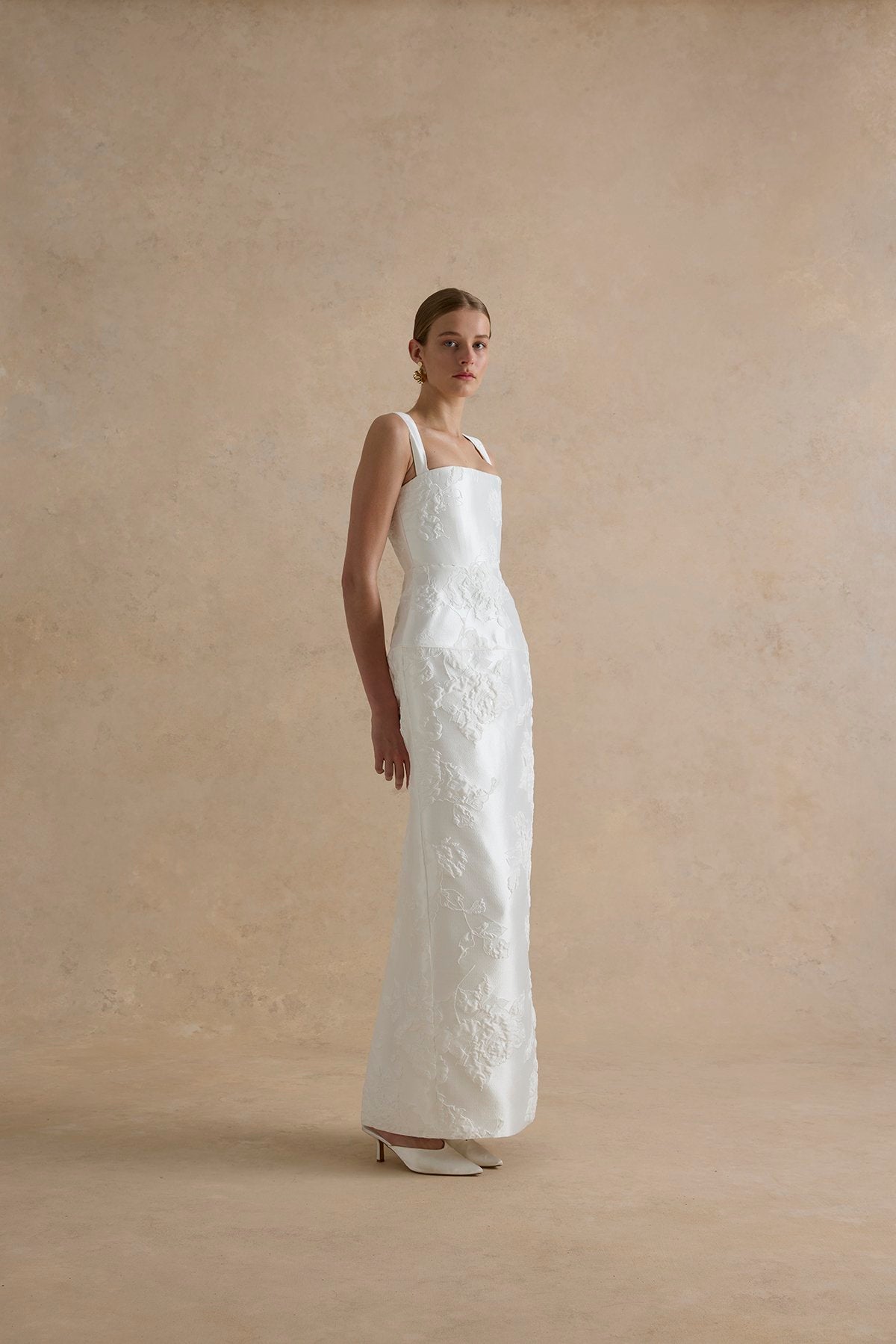 Woman wearing a white lace wedding dress against a plain background