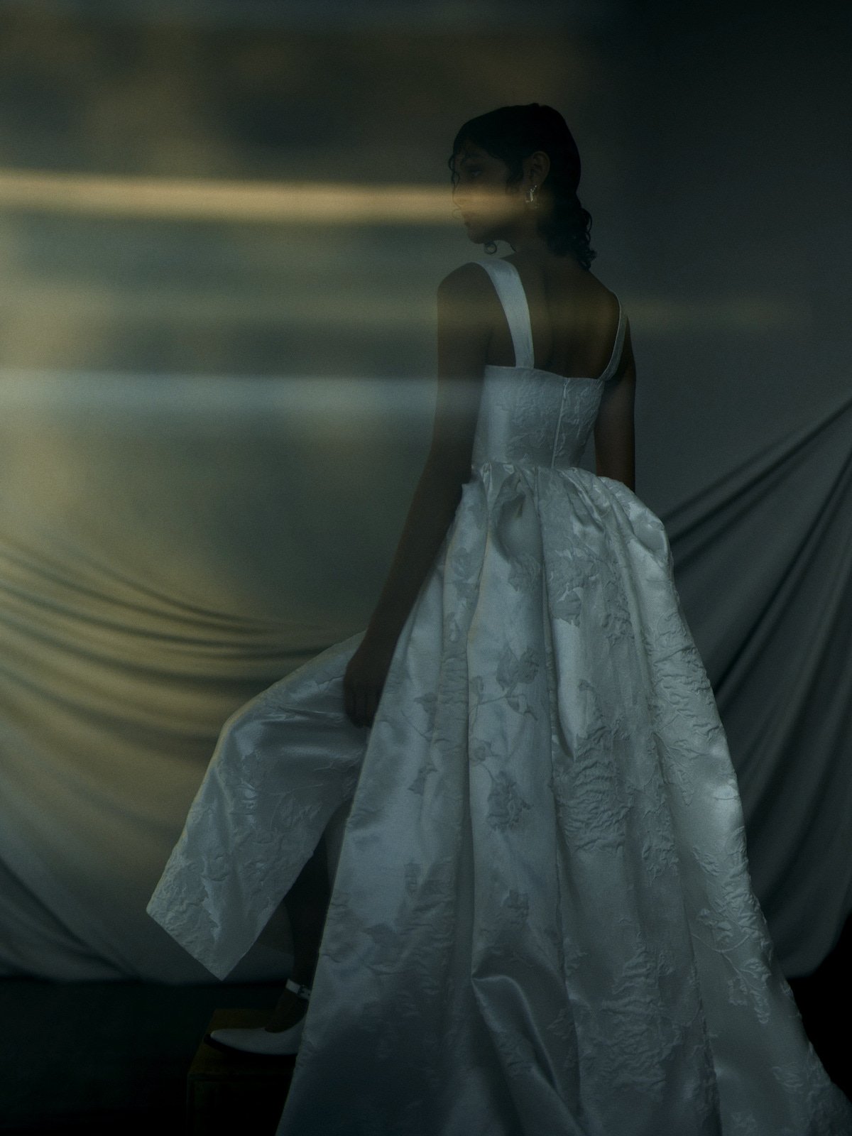 Woman in a white dress standing in front of draped fabric with a dark background