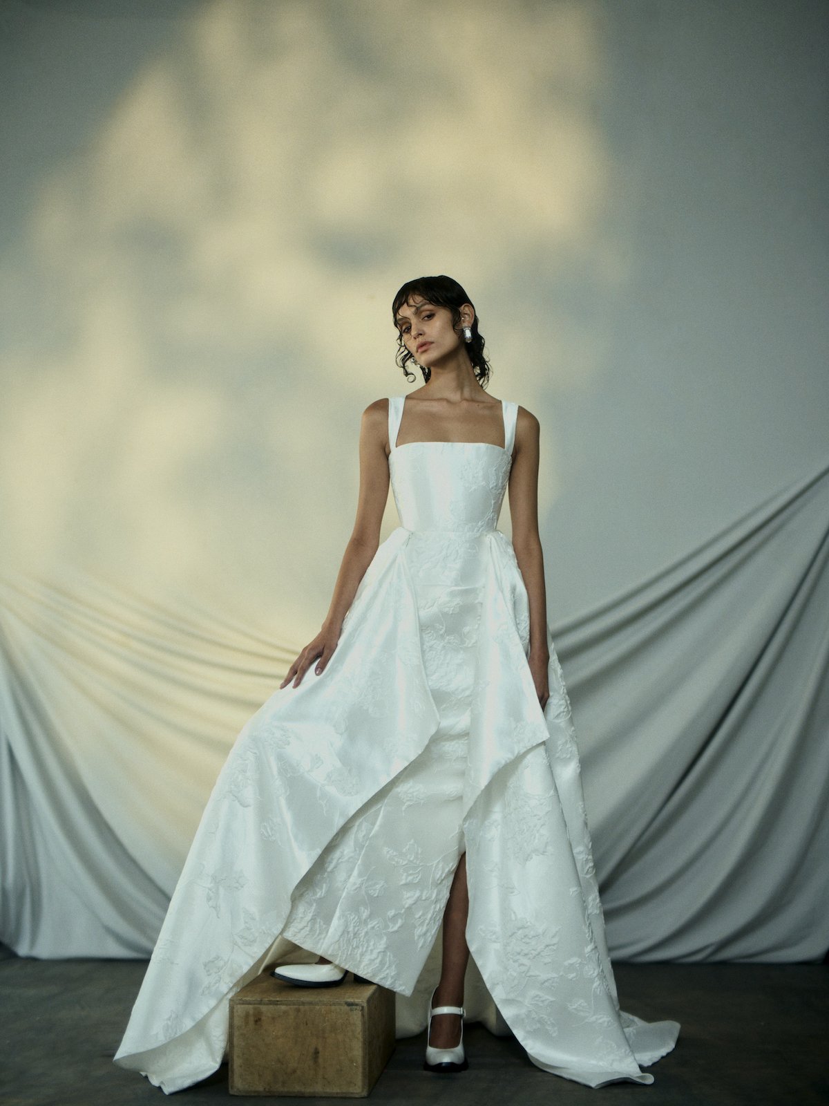 Woman in a white wedding dress standing against a draped fabric background