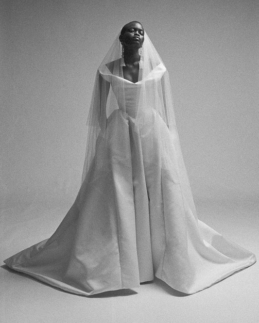 Model wearing the Nova Bagatelle gown with a cinched waist and full skirt, styled with a sheer veil in black and white