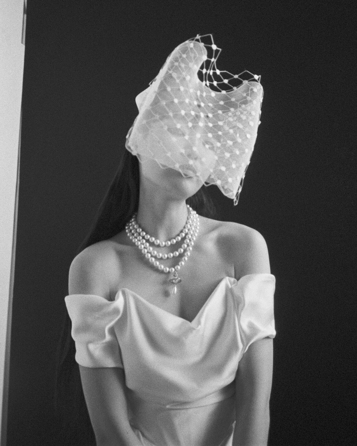 Black and white photo of model wearing Nova Cocotte off-shoulder gown with layered pearl necklace and netted face veil