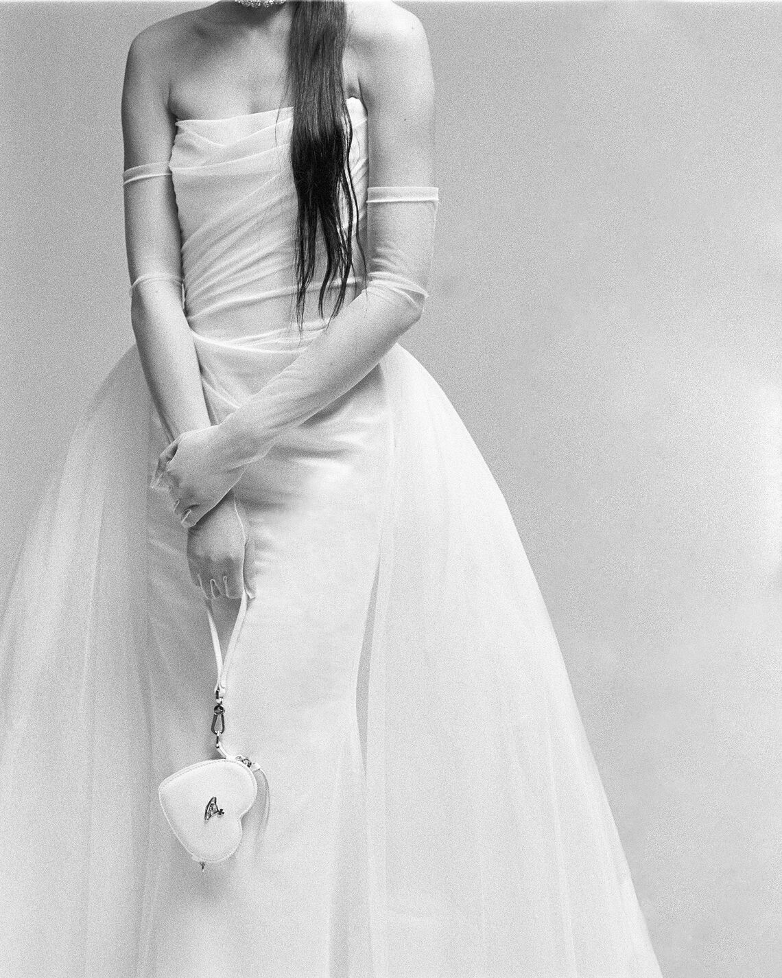 Woman in a strapless white wedding dress holding a heart-shaped object against a plain background