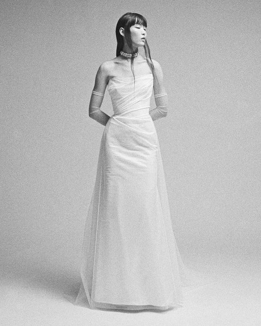 Woman wearing a long, elegant white dress against a plain background