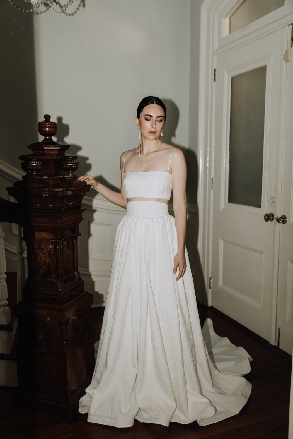 Model wearing the Oscar Skirt with a matching white cropped top in an elegant indoor setting with wooden staircase details