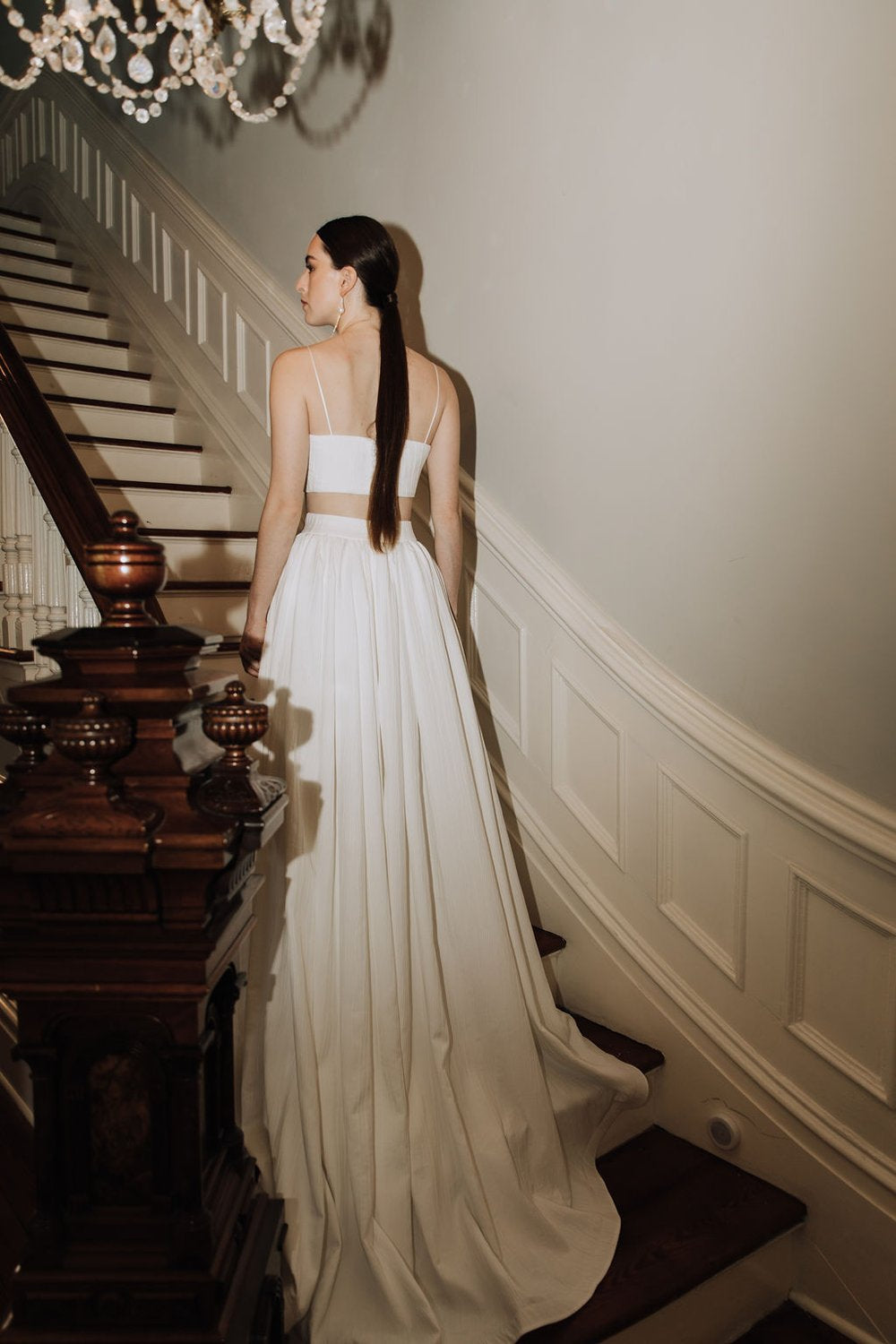 Model wearing the Oscar skirt with a flowing train and simple white cropped top standing on a vintage staircase