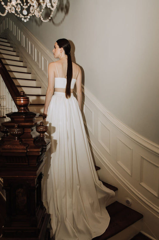 Model wearing the Oscar skirt with a flowing train and simple white cropped top standing on a vintage staircase